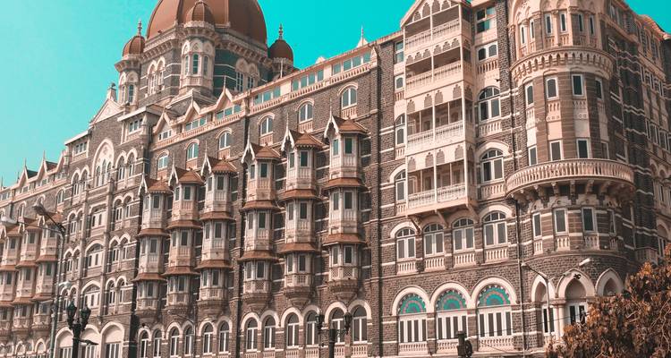 Hotel Palacio Taj Mahal icónico en Mumbai con cúpulas ornamentadas y ventanas arqueadas bajo un cielo turquesa.