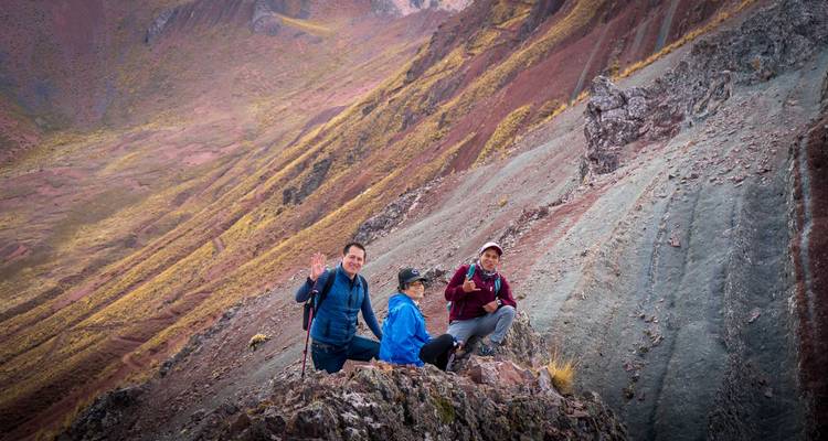 Tres senderistas sonriendo posando en una formación rocosa dentada de una cresta colorida en los Andes.