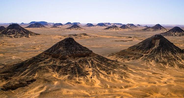 Vista aérea de colinas volcánicas cónicas negras elevándose desde amplias llanuras desérticas arenosas