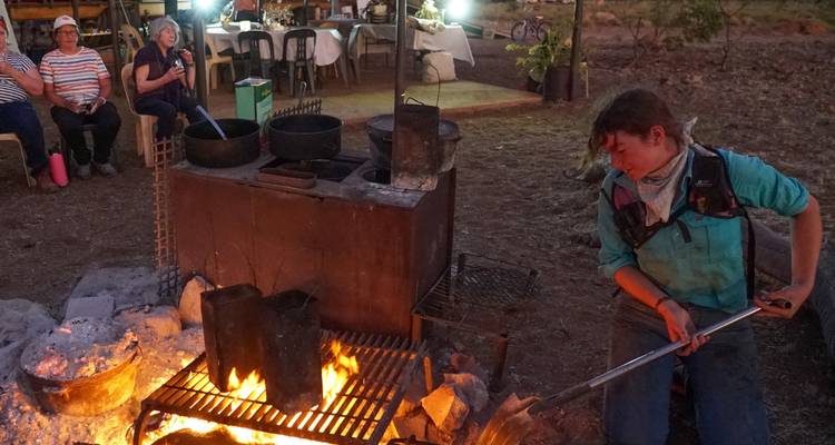 Cuisine du camp de l'Outback où un guide s'occupe d'un feu tandis que les clients observent depuis leurs tables.