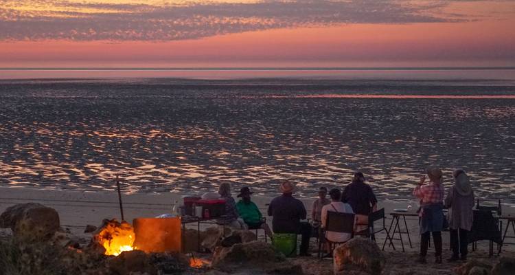 Les voyageurs sont assis autour d'un feu de camp sur la plage et regardent un coucher de soleil orange éclatant sur les vasières.