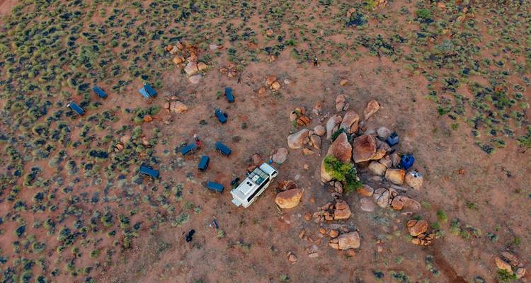 Vue aérienne d'un véhicule 4x4 isolé et de sacs de couchage dispersés parmi les rochers rouges du désert.