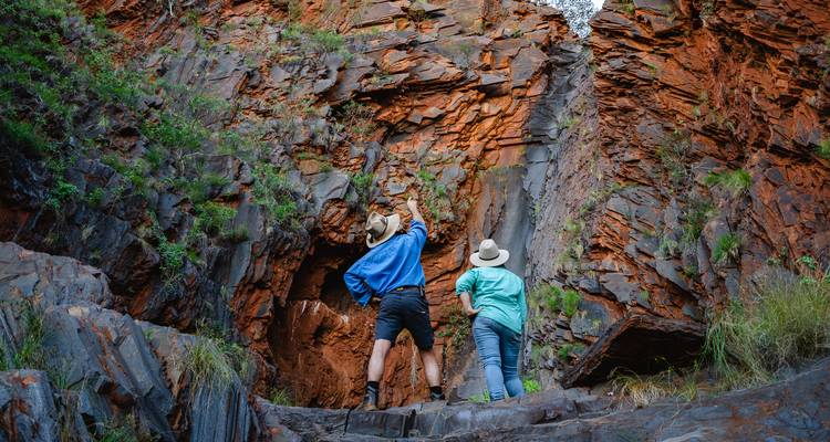 Des voyageurs examinant d'imposantes parois rocheuses orange dans une gorge désertique accidentée.