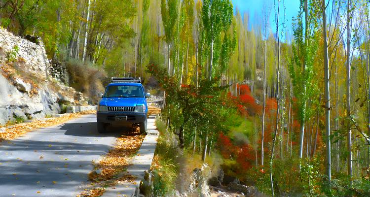 Véhicule 4x4 garé sur une route de montagne étroite entourée de feuillage automnal aux couleurs vives.