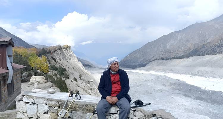 Un homme vêtu d'équipement de randonnée se repose sur un mur de pierre surplombant une large vallée glaciaire entourée de pics nus.