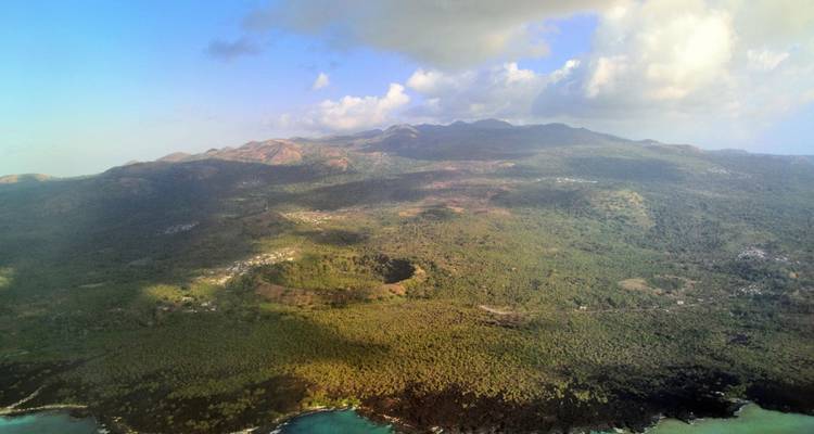 Toma aérea de un paisaje volcánico verde que desciende hacia calas color turquesa y costas de lava negra.