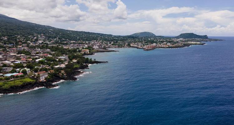 Una impresionante vista aérea de la costa mostrando un pueblito tropical lleno de vida y dos puntas de tierra que se adentran en el mar azul profundo.