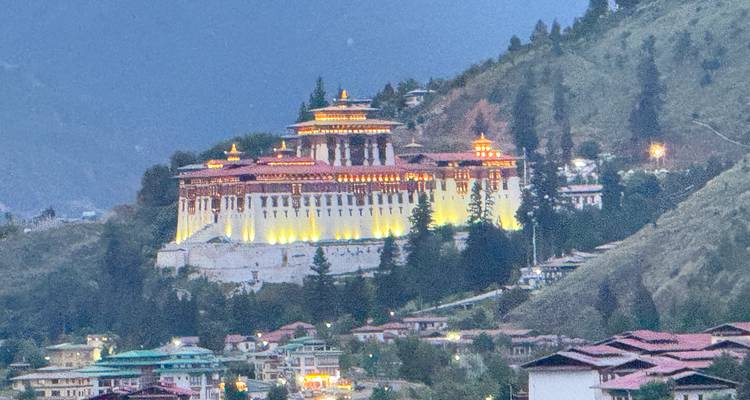 Punakha Dzong gloedt op in warm licht bij zonsondergang, genesteld tegen een beboste heuvel.
