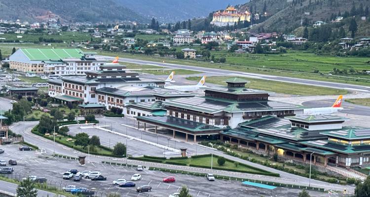 Luchtfoto van de terminalgebouwen van luchthaven Paro met start- en landingsbaan en dal landschap; dzong zichtbaar op een heuvel.