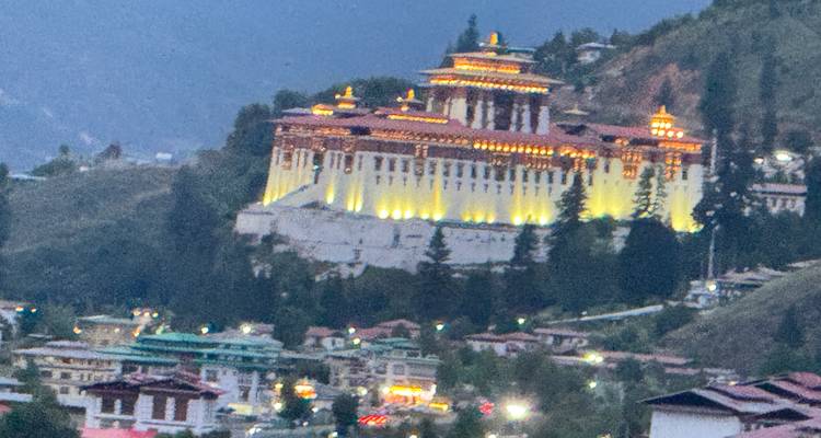 Ingezoomde avondfoto van een fel verlicht dzong op een heuvel met duidelijk zichtbare beeldruis.