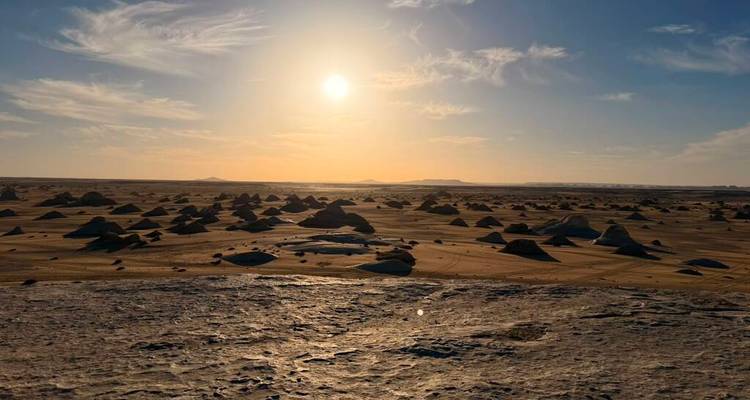 El sol bajo sobre una llanura desértica inmensa punteada de montículos de roca moldeados por el viento bajo nubes tenues.