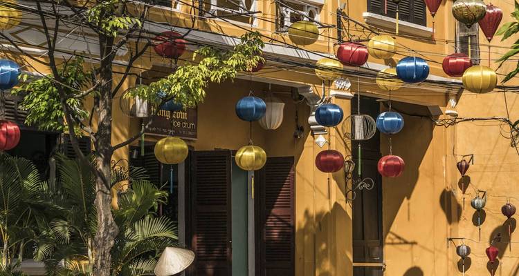 Faroles coloridos colgando de un edificio histórico de color amarillo mostaza en el casco antiguo de Hoi An.