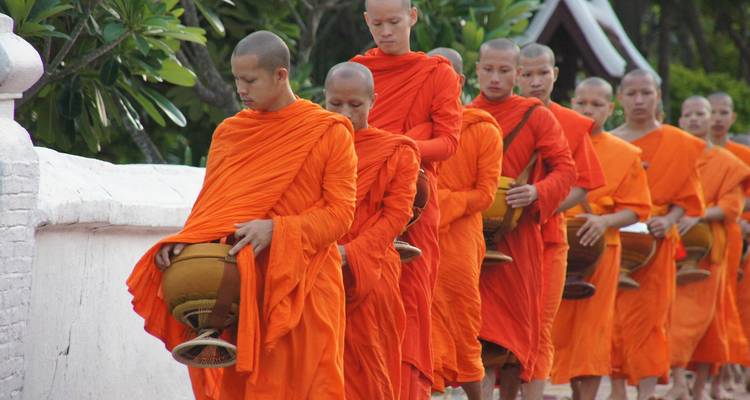 Een stoet van boeddhistische monniken in felle oranje gewaden loopt achter elkaar in een traditionele aalmoezenieceremonie.