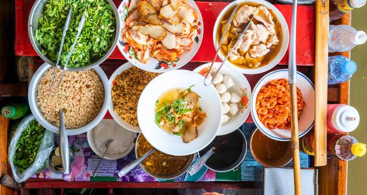 Bovenaanzicht van Thaise gerechten en verse ingrediënten op een tafel in een eetentje op een drijvende markt.