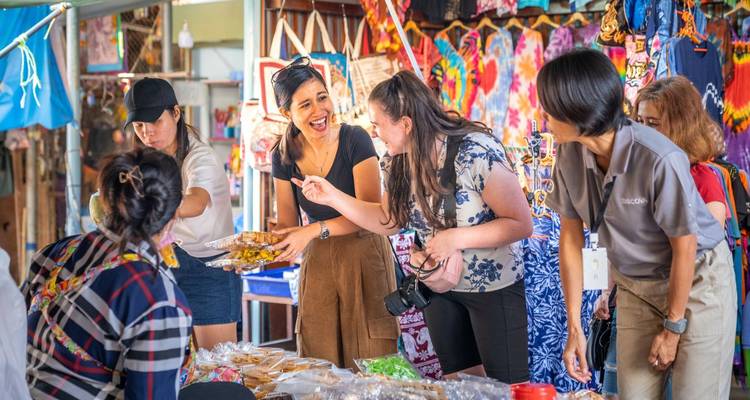 Groep reizigers die lachen en snacks proeven bij een kleurrijke Thaise marktstand.