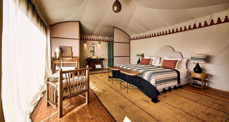 Chambre élégante de style safari avec tentes, lits jumeaux, tapis tissés et lumière naturelle filtrant à travers les parois en toile.