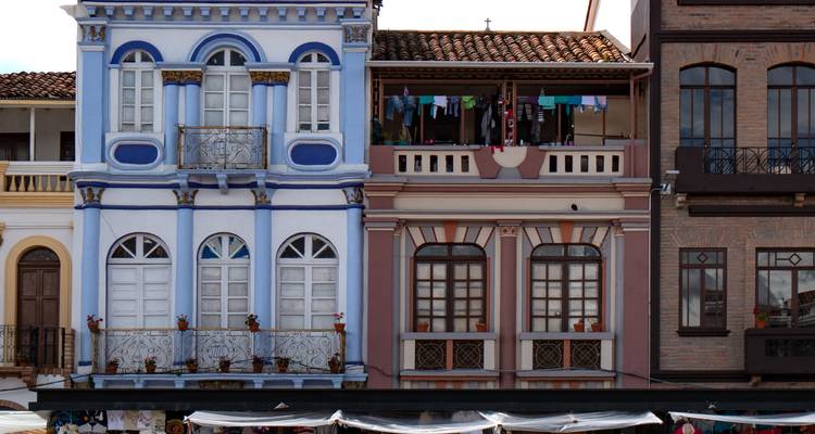 Rangée de façades coloniales aux couleurs pastel avec balcons et fenêtres en arc.
