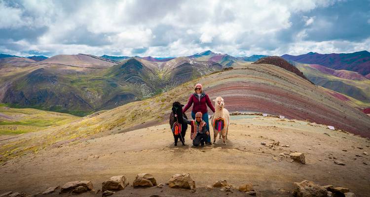 Bezoekers die poseren met twee alpaca's tegen de spectaculaire achtergrond van Rainbow Mountain.