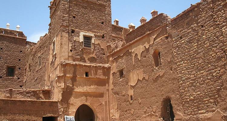 Close view of rugged stone kasbah walls and arched entrance under a bright sky.