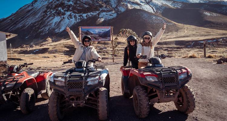 Drie enthousiaste vrouwen op quad bikes steken hun armen omhoog voor met sneeuw bestoven Andes-pieken.
