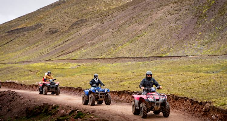 Een groep rijders manoeuvreert met quad bikes langs een onverharde weg omzoomd door kale Andese hellingen.