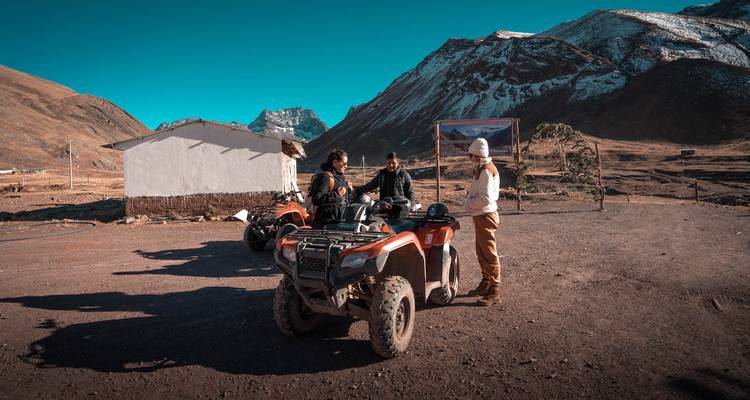 Reizigers verzamelen zich bij quad bikes op een afgelegen basis met sneeuwwitte Andean bergkammen op de achtergrond.