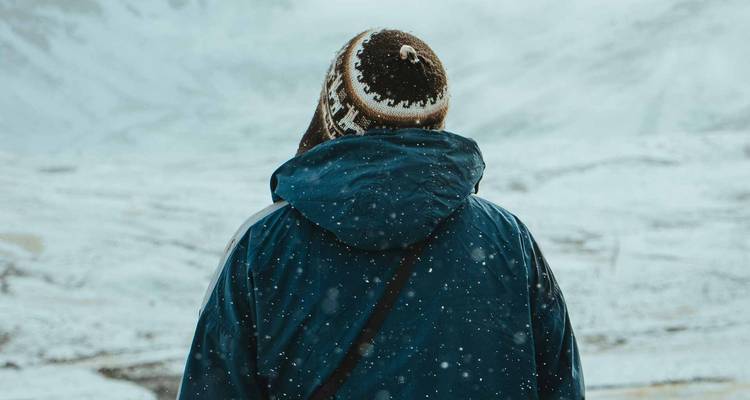 Achteraanzicht van reiziger in sneeuwval met wollen Andes-muts tegen sneeuwlandschap.