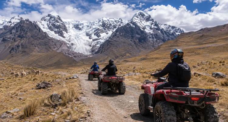 Rij van ATV-rijders die zich naar imposante, met gletsjers bedekte bergen begeven op een ruw zandpad.