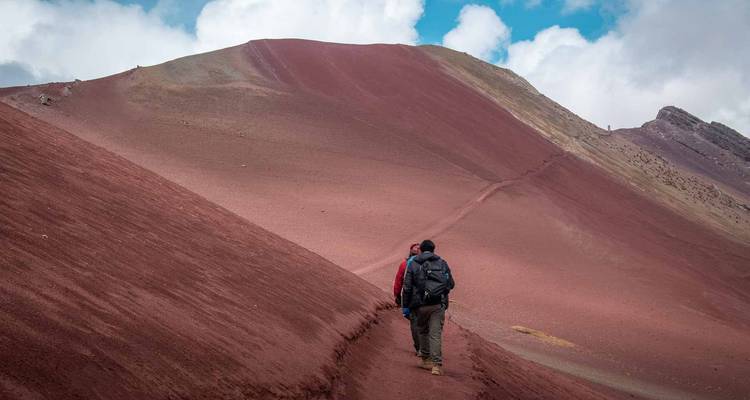 Wandelaars lopen over een smal pad op de indrukwekkende rode helling van Rainbow Mountain.