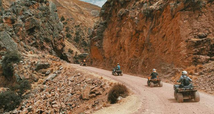 Groepsrit met ATVs door een steil rood canyon met ruige rotsachtige wanden.