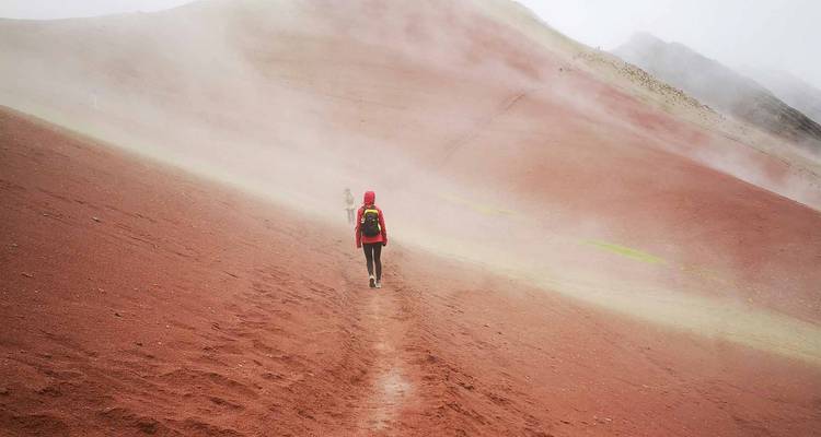 Wandelaars bewegen zich door mist die over de rode zandhellingen van Rainbow Mountain uitwaaiert.