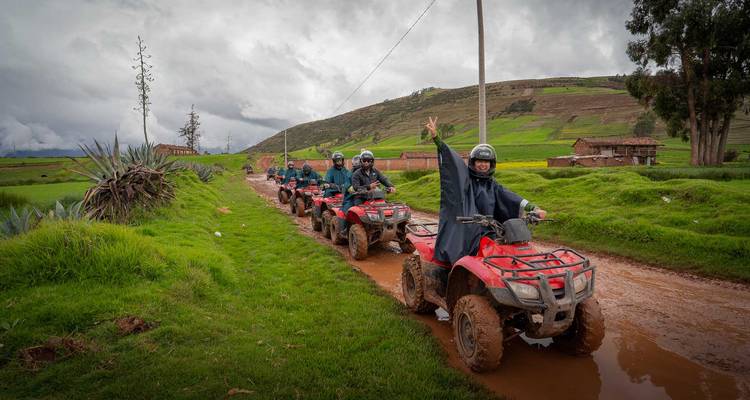 Gelukkige groep op ATV's geeft vredesteken terwijl ze over een modderige plattelandsweg rijden die omgeven is door velden.