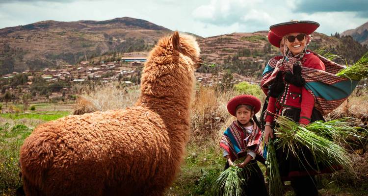 Andaanse vrouw en kind in kleurrijke traditionele kleding die een fluffy alpaca voedt met bergdorpje-achtergrond