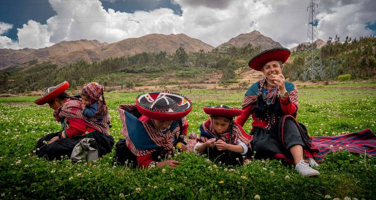 Vrouwen en kinderen in kleurrijke Quechua-kleding die ontspannen en kruiden proeven terwijl zij in een groen veld zitten met bergen op de achtergrond