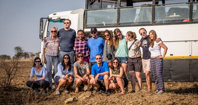 Grupo de turismo grande posando frente a un camión para expediciones en una llanura polvorienta