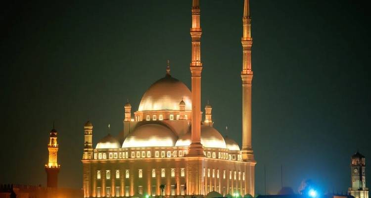 Een verlichte moskee en minaretten gloeien tegen de donkere nachtelijke hemel in Caïro's skyline.