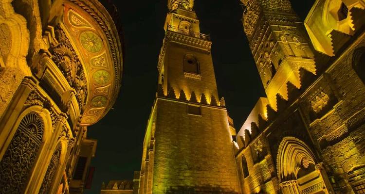 Dramatisch opwaarts uitzicht op oude minaretten en steenwerk badend in gouden nachtverlichting.