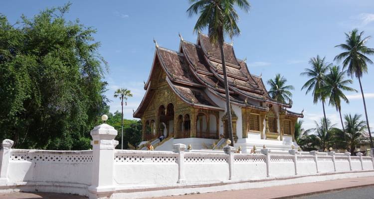 Temple laotien élégant aux toits ornementés et aux murs blancs, entouré de palmiers et d'un ciel bleu