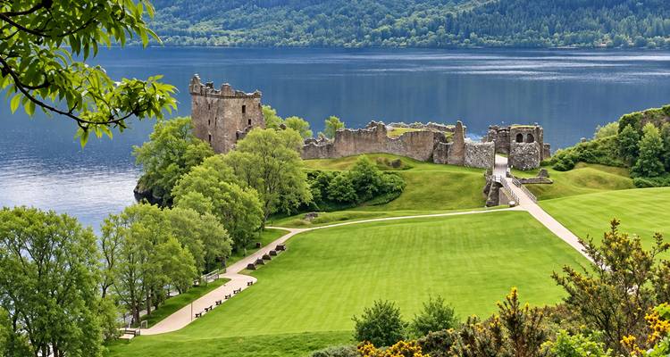Les pelouses verdoyantes et les versants boisés encadrent les vestiges de pierre du château d'Urquhart s'étendant dans le Loch Ness tranquille.