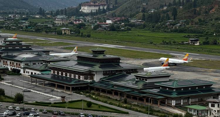 Luchthaventerminal van Paro met Drukair-vliegtuigen en Paro Dzong op de heuvel erachter