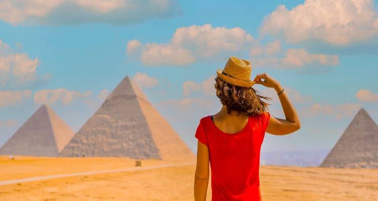 Jonge vrouw in rode jurk die naar de Piramides van Giza kijkt tegen een blauwe lucht