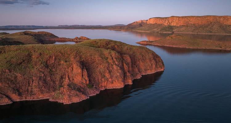 La lueur du coucher de soleil aérien surplombant les falaises rouges et les eaux calmes du vaste lac Argyle.