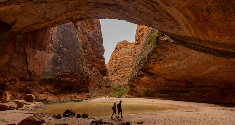 Des randonneurs marchant sous une imposante arche de grès naturelle à l'intérieur des gorges de la chaîne de Bungle Bungle.