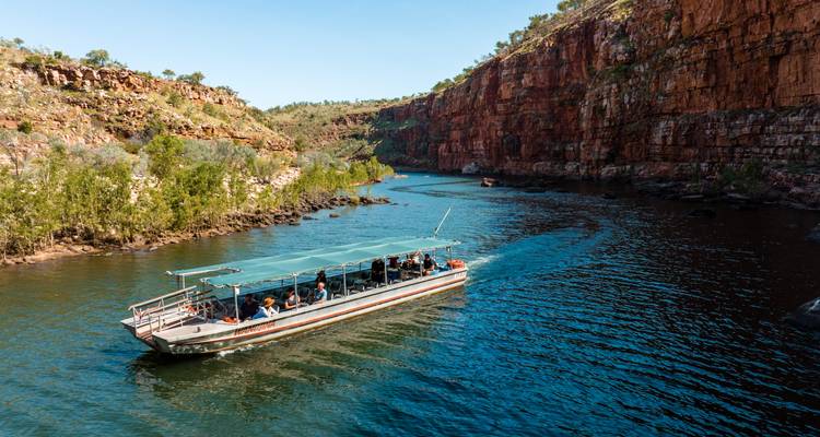 Un barco de turismo techado lleno de pasajeros navega a través de un estrecho cañón con acantilados rojos escarpados y agua de color esmeralda.