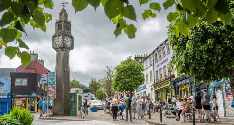 Place animée d'une petite ville irlandaise avec une tour horloge, des cafés et des foules profitant d'une journée d'été.
