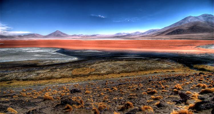 Vaste désert d'haute altitude avec un magnifique salant rouge vif, des pics lointains et un ciel dramatique.