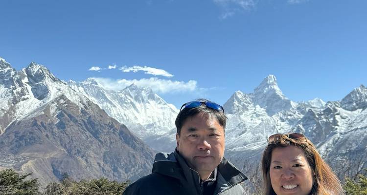 Twee trekkingsliefhebbers poseren met uitzicht op het met sneeuw bedekte Everest-gebergte onder een diepblauwe hemel.