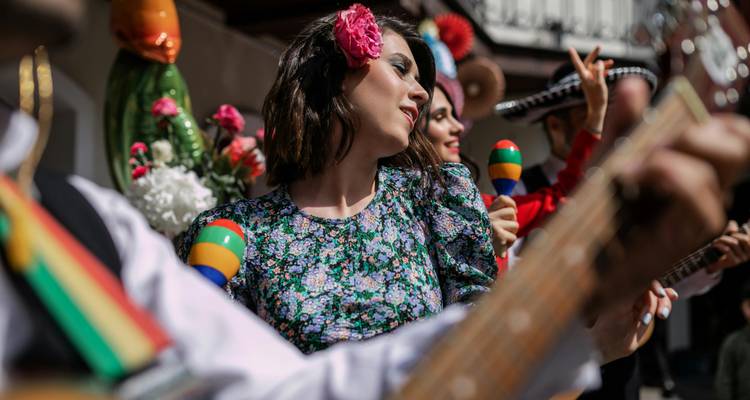Des musiciens en tenue traditionnelle colorée jouent de la guitare et des maracas en dansant en plein air lors de festivités.