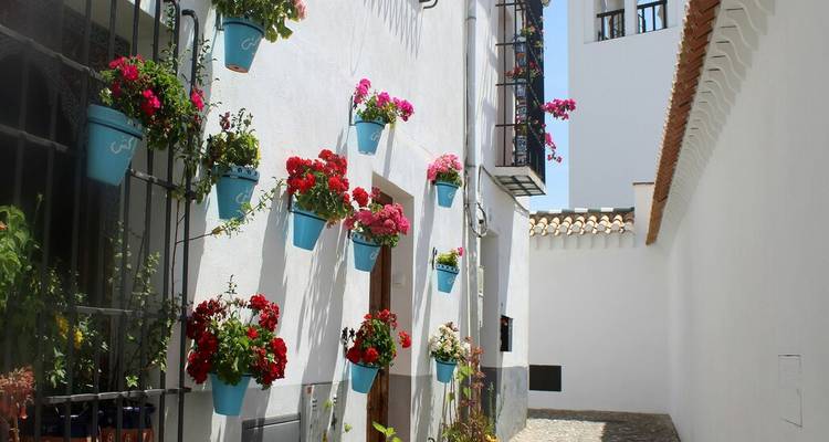 Ruelle blanche étroite andalouse décorée de pots de fleurs colorés suspendus aux murs.