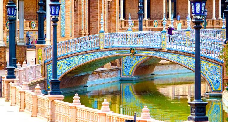 Pont orné de carreaux de céramique traversant le canal à la Plaza de España de Séville avec des reflets dans l'eau.